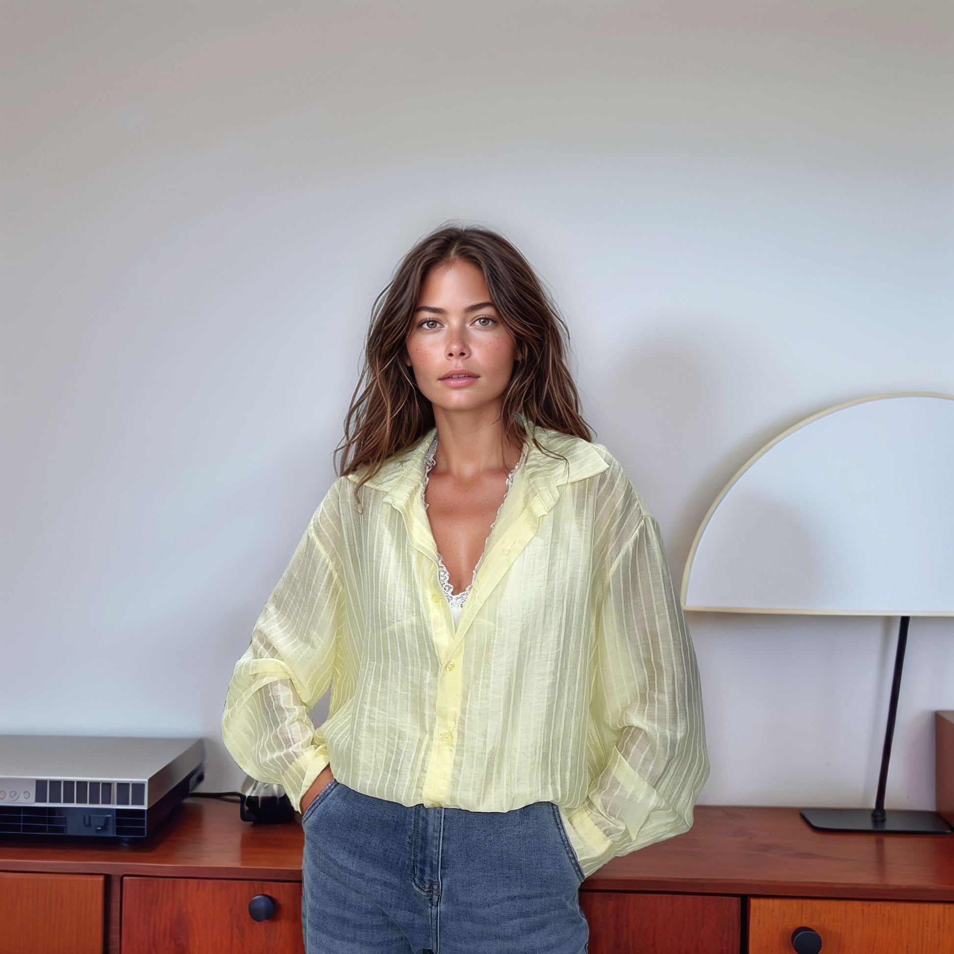 Modelo de cabelos castanhos ondulados veste a Blusa Olívia na cor amarela suave, destacando o caimento fluido do tecido tencel e as mãos nos bolsos de uma calça jeans.