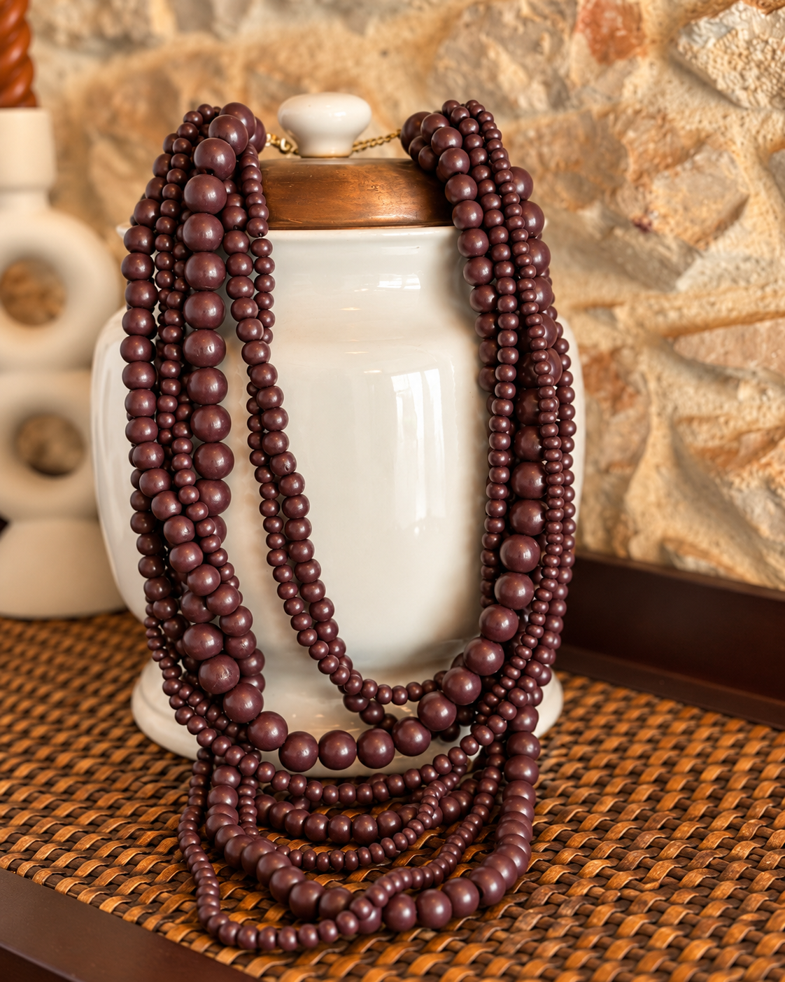 Colar de bolas castanho com múltiplas fiadas de diferentes tamanhos, pousado sobre uma jarra branca. Josephine.