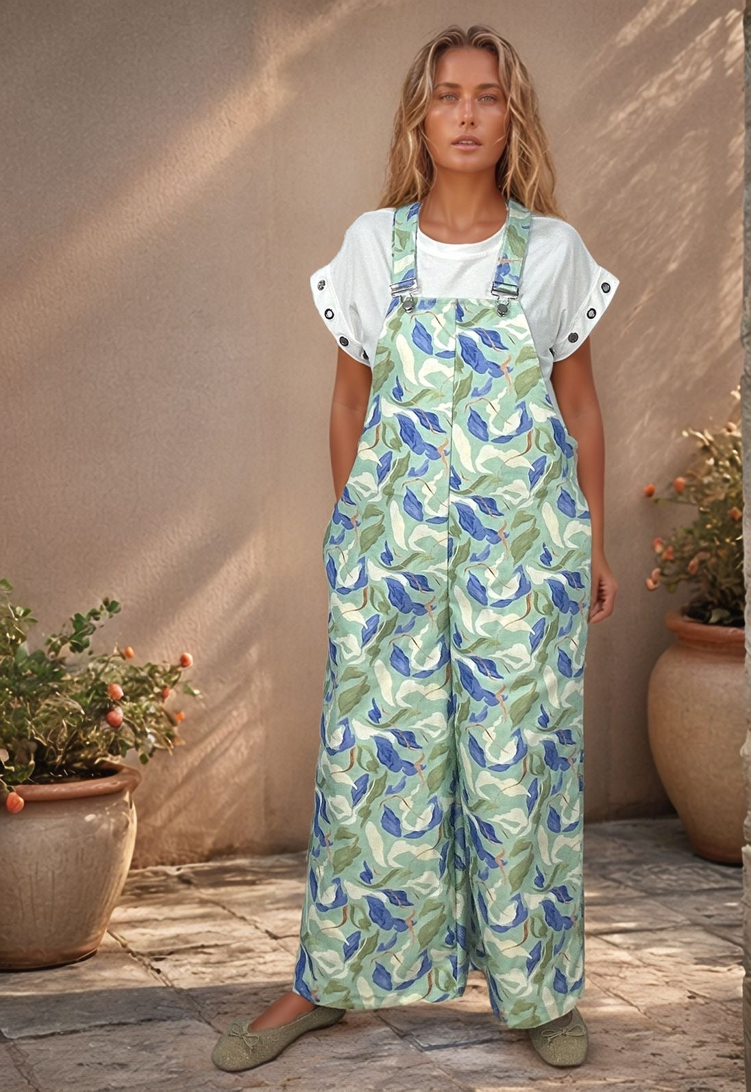 Modelo de cabelo loiro e silhueta curvilínea veste jardineiras Eden com estampa botânica verde e azul.