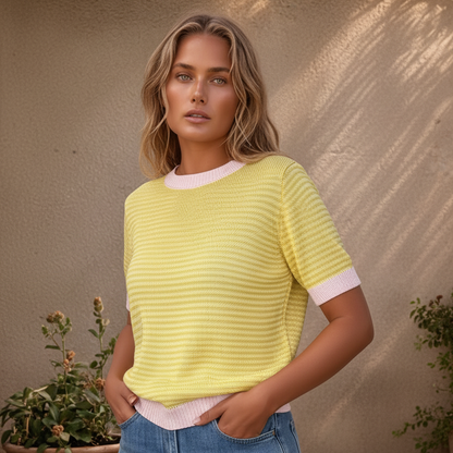 Mulher de cabelos castanhos e corpo curvilíneo vestindo blusa de tricô amarela e rosa com calça jeans