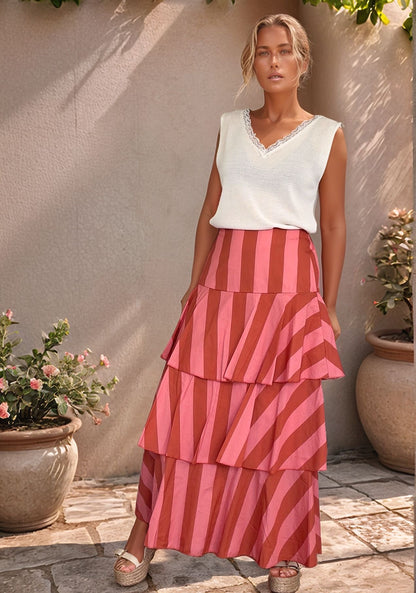 Modelo loira posando de frente com saia de algodão de folhos em listras rosa e terracota combinada com top branco e sandálias de cunha